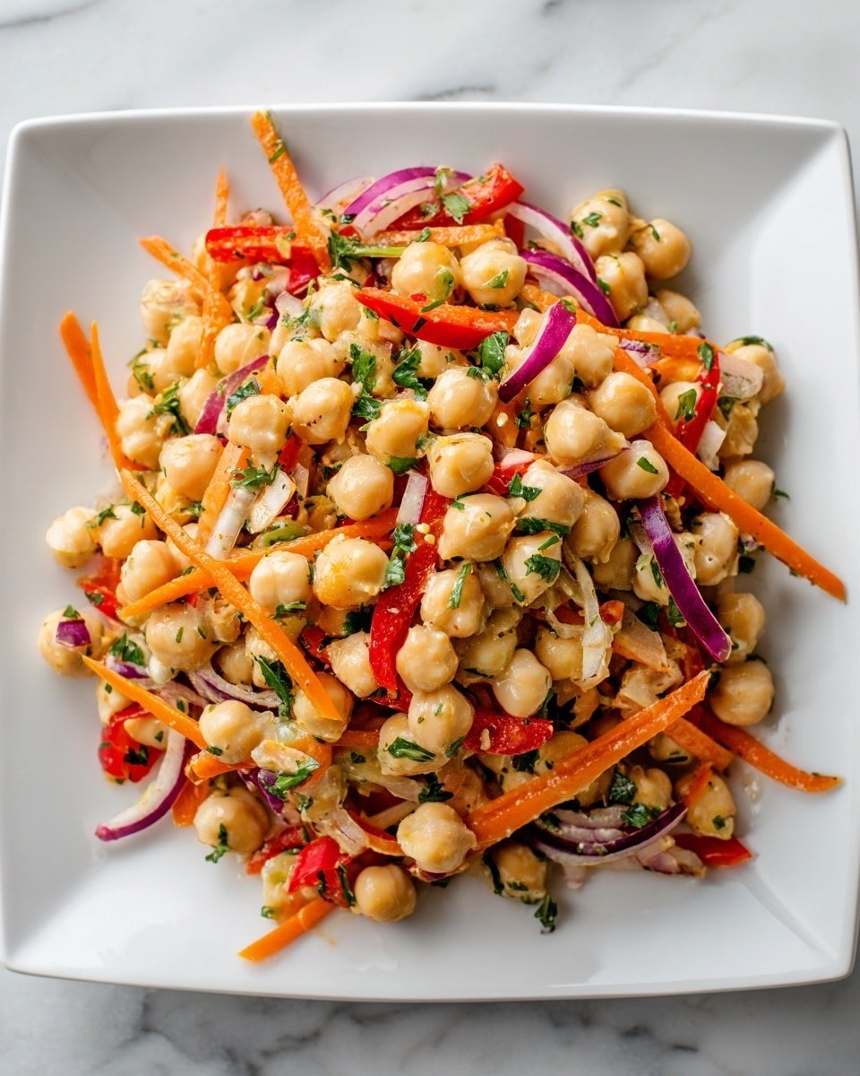 The image shows a close-up of a colorful chickpea salad served on a white square plate. The salad has one main layer with creamy beige chickpeas scattered throughout, mixed with thin strips of bright orange carrots, red bell peppers, sliced purple onions, and chopped green cilantro, all evenly spread. The salad looks fresh with a slight shine, indicating a light dressing. The plate is placed on a white marbled surface. The photo taken with an iphone --ar 4:5 --v 7 — Crunchy Thai Chickpea Salad, Thai chickpea salad, healthy chickpea salad, vegan Thai salad, easy Thai salad recipe